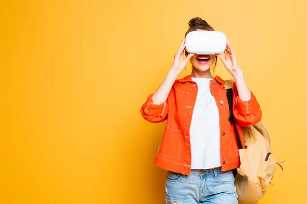 Estudiante emocionado con mochila usando auriculares vr sobre fondo amarillo - foto de stock