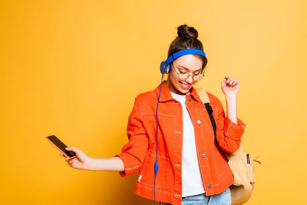 Studente allegro in cuffie che tengono smartphone su sfondo giallo — Foto stock