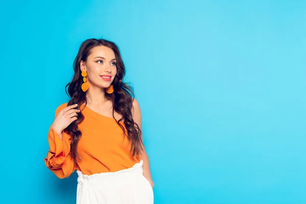 Belle, élégante fille touchant les cheveux et regardant loin sur fond bleu — Photo de stock