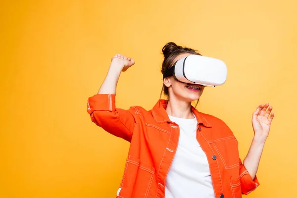 Sourire fille gestuelle tout en utilisant vr casque isolé sur jaune — Photo de stock