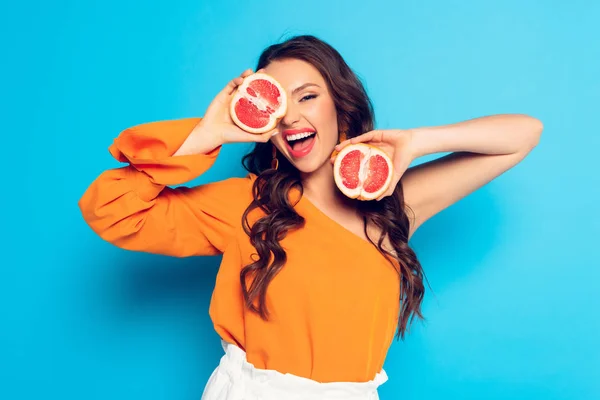 Excitada chica cubriendo el ojo con la mitad de piña madura sobre fondo azul - foto de stock