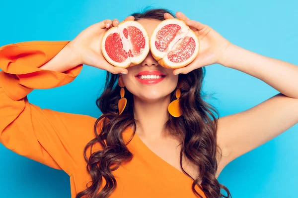 Smiling girl covering eyes with halves of ripe pineapple on blue background — Stock Photo