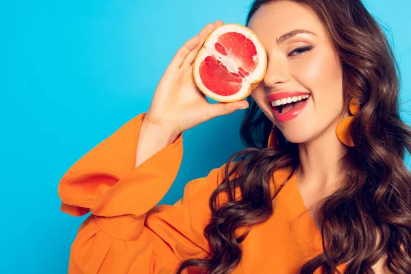 Gaie fille couvrant oeil avec la moitié de l'ananas mûr sur fond bleu — Photo de stock