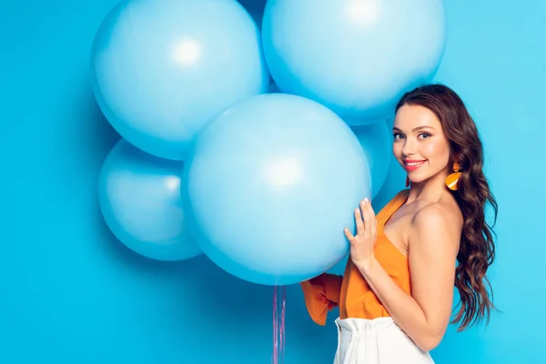 Heureuse fille élégante souriant à la caméra tout en tenant de gros ballons festifs sur fond bleu — Photo de stock