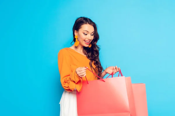 Привлекательная возбужденная девушка смотрит в сумку для покупок на голубом фоне — стоковое фото