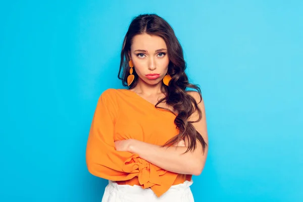 Offended, pouting girl looking at camera while standing with crossed arms on blue background — Stock Photo