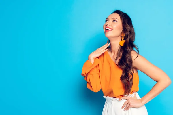 Excitada chica de moda mirando hacia otro lado mientras sostiene la mano en la cadera sobre fondo azul - foto de stock