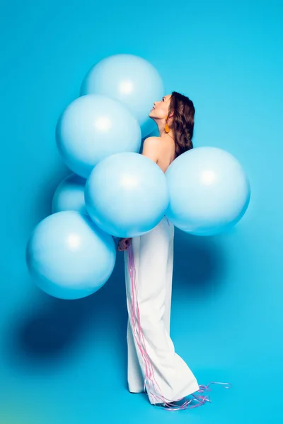 Vue pleine longueur de jeune femme élégante avec de gros ballons festifs sur fond bleu — Photo de stock