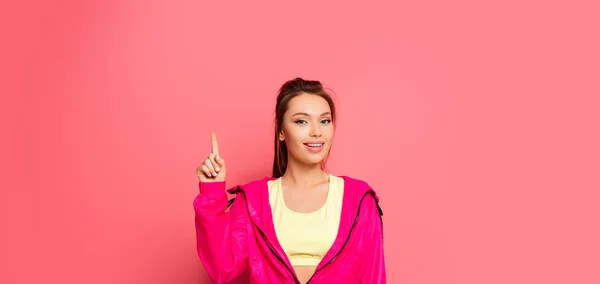 Panoramic shot of young smiling sportswoman showing idea gesture on pink background — Stock Photo