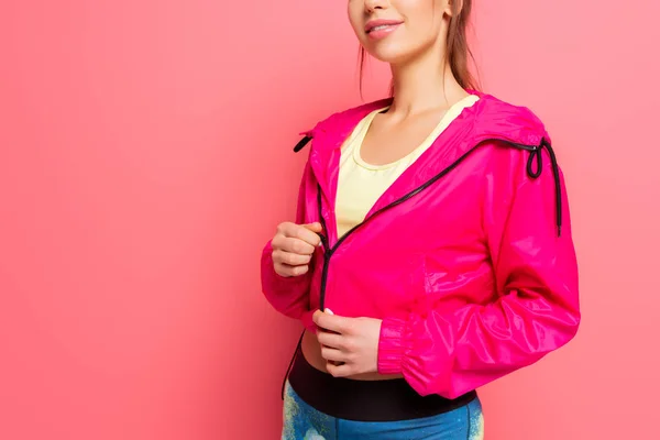 Vista ritagliata di giovane sportiva sorridente in giacca a vento rosa su sfondo rosa — Foto stock