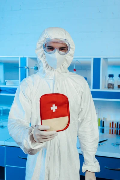 Científico en traje de materiales peligrosos y gafas que sostiene el botiquín de primeros auxilios - foto de stock