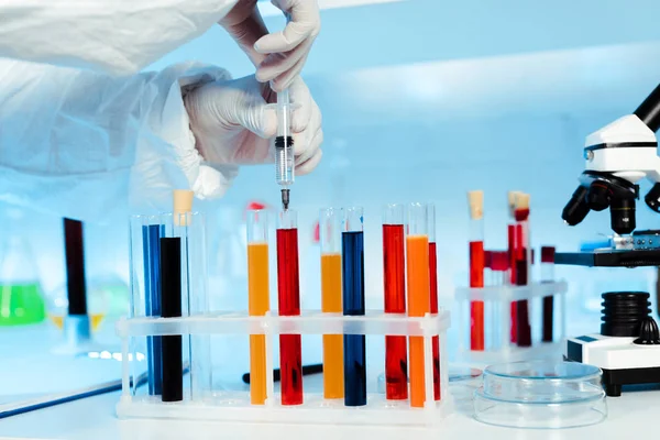 Cropped view of scientist holding syringe near test tubes with samples — Stock Photo