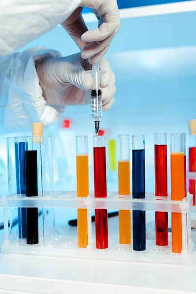 Cropped view of scientist in latex gloves holding syringe near test tubes with samples — Stock Photo