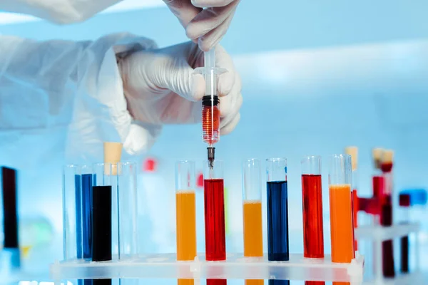 Cropped view of scientist in latex gloves holding syringe near test tubes — Stock Photo