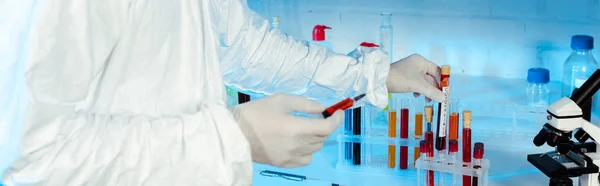 Tiro panorâmico do cientista em luvas de látex segurando seringa perto de tubos de ensaio — Fotografia de Stock