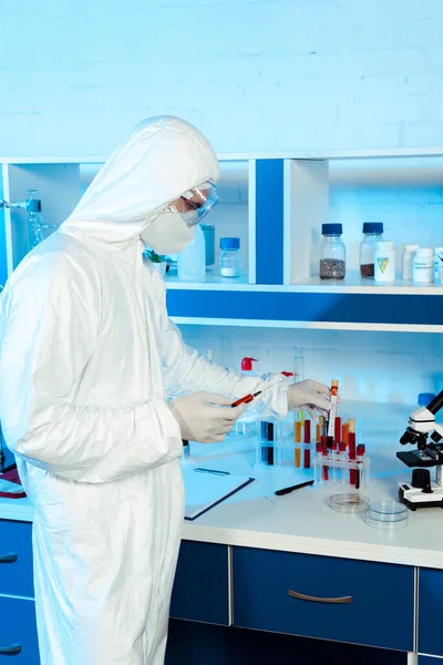 Científico en guantes de látex con jeringa y tubo de ensayo con letras de coronavirus - foto de stock