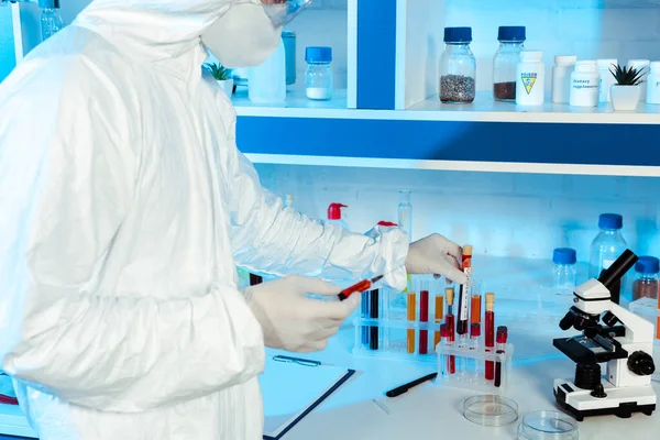 Vista recortada del científico en guantes de látex que sostienen la jeringa y el tubo de ensayo con letras de coronavirus - foto de stock