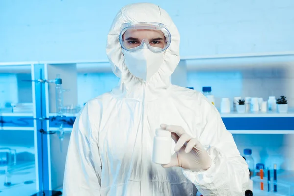 Científico en traje de materiales peligrosos y gafas que sostienen la botella en laboratorio - foto de stock