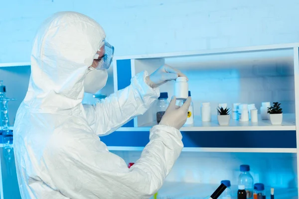 Scientifique en gants et lunettes de latex regardant bouteille en laboratoire — Photo de stock