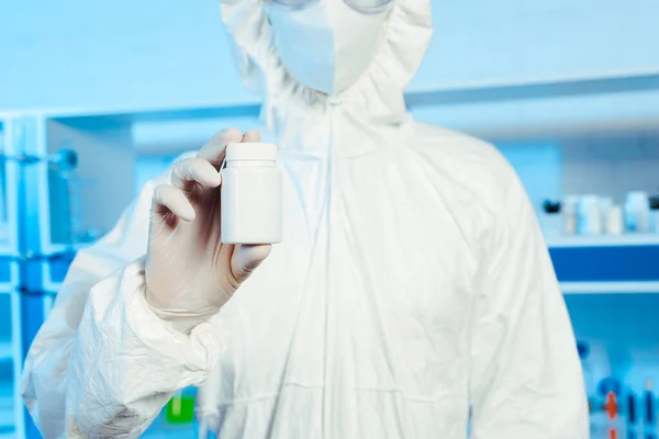 Vista recortada del científico en traje de materiales peligrosos que sostiene la botella en el laboratorio - foto de stock