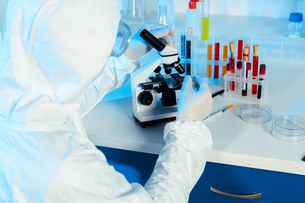 Científico en traje de materiales peligrosos cerca del microscopio en laboratorio - foto de stock