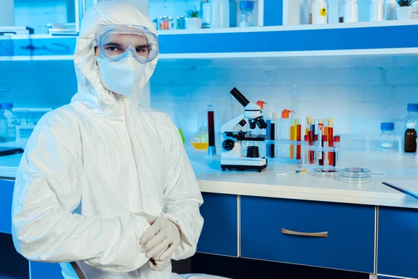 Учёный в защитном костюме и очках, стоящих возле микроскопа — стоковое фото