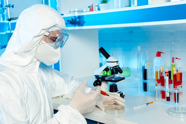 Scientist in hazmat suit and goggles holding syringe near test plate — Stock Photo