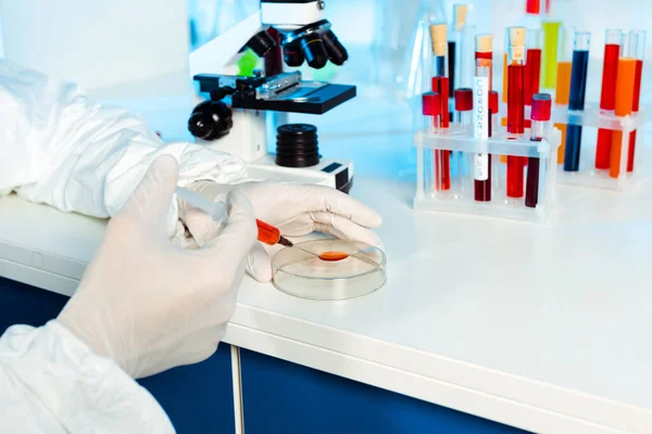 Cropped view of scientist in latex gloves holding syringe near glass test plate — Stock Photo