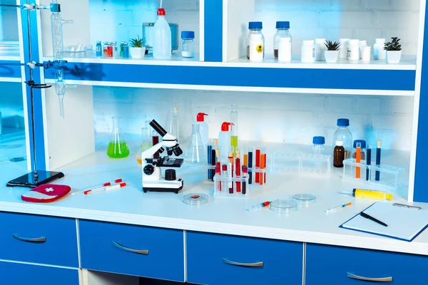 Frascos, tubos de ensayo y botellas cerca del microscopio en laboratorio moderno - foto de stock