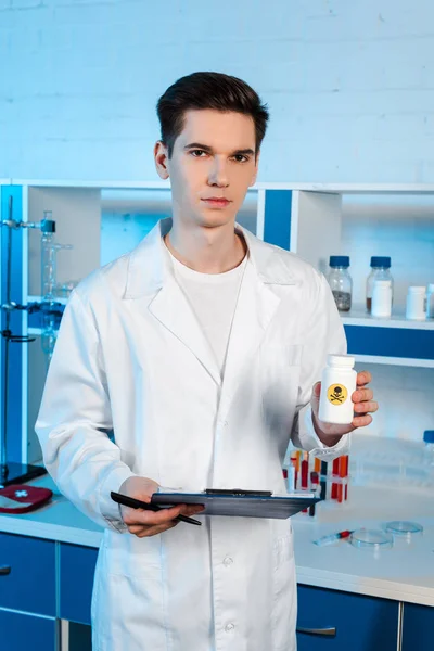 Красивый ученый держит планшет и бутылку с токсичным символом — стоковое фото