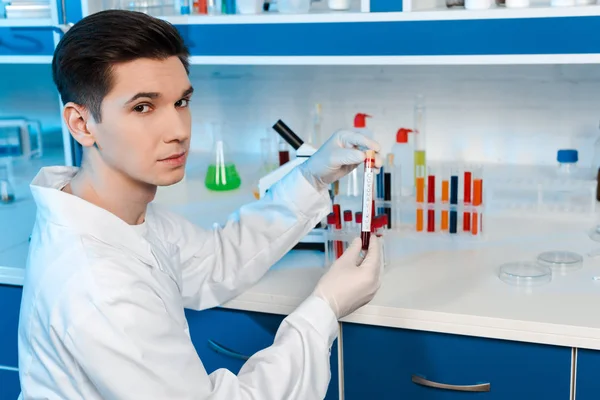 Handsome scientist in latex gloves holding sample with coronavirus lettering — Stock Photo