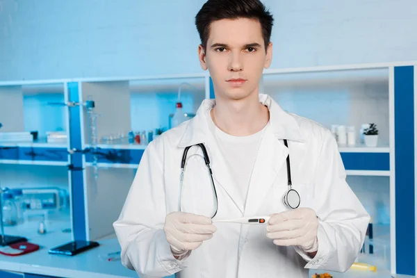 Handsome scientist in latex gloves holding digital thermometer — Stock Photo