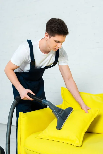 Beau nettoyeur en salopette enlever la poussière sur l'oreiller avec aspirateur — Photo de stock