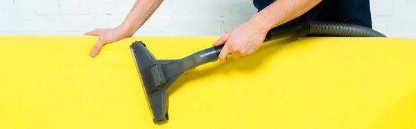 Panoramic shot of cleaner removing dust on sofa with vacuum cleaner — Stock Photo