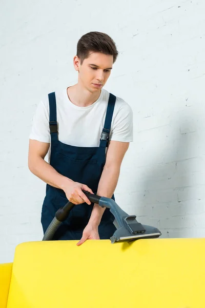 Handsome cleaner removing dust on sofa with vacuum cleaner — Stock Photo