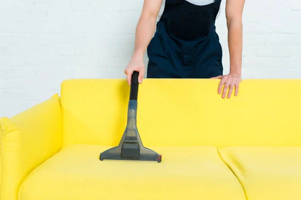 Ausgeschnittene Ansicht eines Reinigers in Uniform, der Staub auf dem Sofa mit Staubsauger entfernt — Stockfoto
