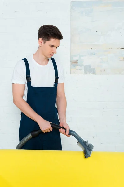 Young cleaner dry cleaning modern sofa with vacuum cleaner — Stock Photo