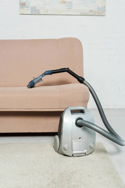 Aspirapolvere su moquette vicino al divano moderno in soggiorno — Foto stock