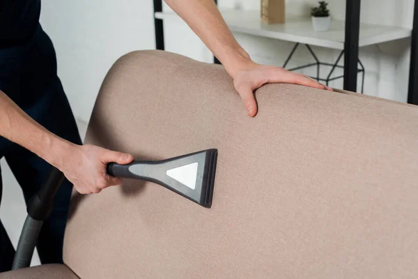 Cropped view of young man cleaning modern sofa with vacuum cleaner — Stock Photo