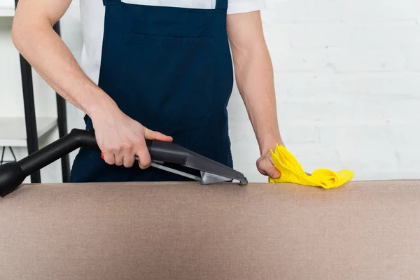 Cropped view of man cleaning sofa with vacuum cleaner and cleaning cloth — Stock Photo