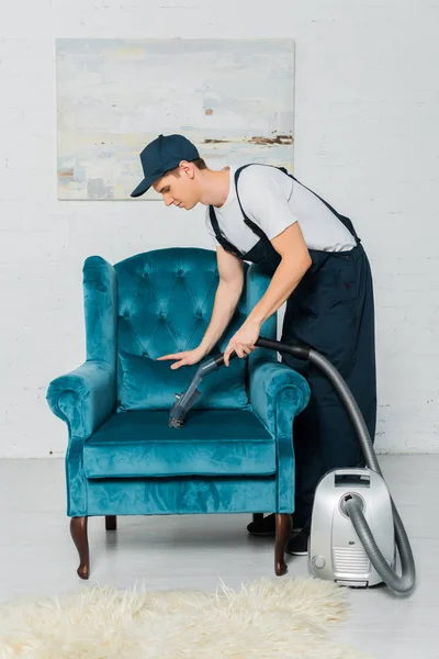 Vista lateral de la limpiadora en la limpieza uniforme sillón moderno con aspiradora - foto de stock