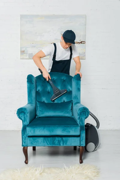 Limpiador en uniforme y la tapa de limpieza moderno sillón con aspiradora - foto de stock