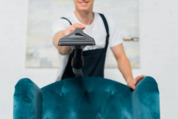 Foyer sélectif de l'aspirateur en main du jeune nettoyeur près du fauteuil moderne — Photo de stock