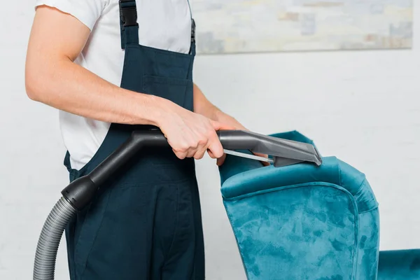 Vue recadrée du nettoyeur en uniforme nettoyage à sec fauteuil bleu avec aspirateur — Photo de stock