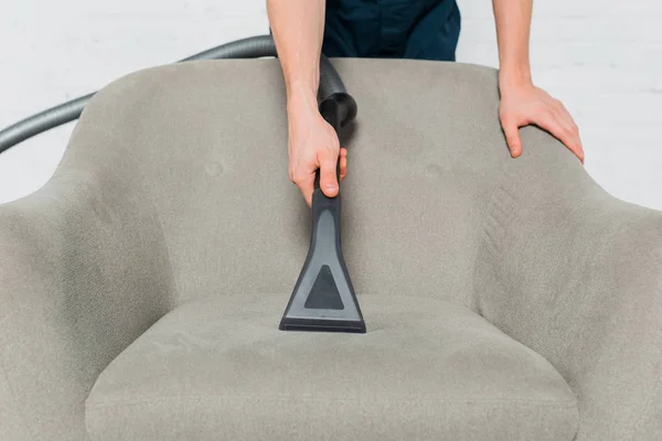 Cropped view of young man dry cleaning armchair with vacuum cleaner — Stock Photo