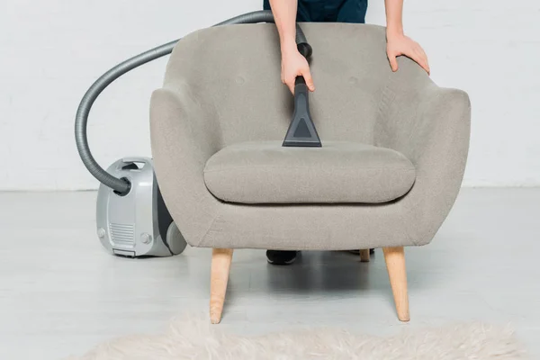 Cropped view of young man dry cleaning armchair with modern vacuum cleaner — Stock Photo