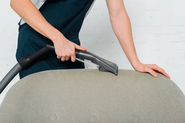 Cropped view of young cleaner dry cleaning armchair with modern vacuum cleaner — Stock Photo