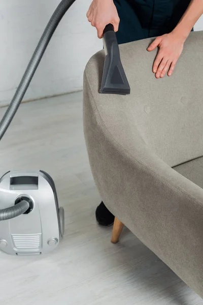 Cropped view of young cleaner dry cleaning armchair with vacuum cleaner in living room — Stock Photo