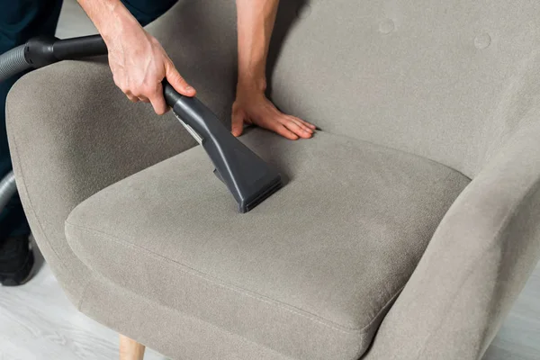 Cropped view of young cleaner washing armchair with vacuum in living room — Stock Photo