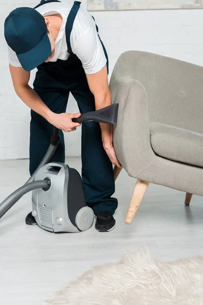 Nettoyeur en uniforme et chapeau fauteuil de lavage avec aspirateur dans le salon moderne — Photo de stock